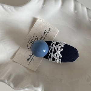 Detail of navy blue hair clip featuring a blue bead and white lace bow on ceramic tray