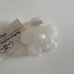 Détail d'une pince à cheveux fleur blanc crème avec fini nacré et texte France handmade