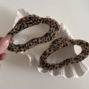 Detailed close-up of two leopard print acetate hair claws in a decorative shell dish