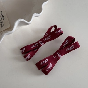 Détail de deux pinces à cheveux à nœuds bordeaux avec texte blanc sur une assiette blanche