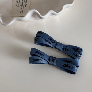 Détail des barrettes à nœud en ruban bleu avec lettrage Alline sur assiette en céramique