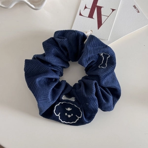 Détail d'un chouchou en velours côtelé bleu marine avec broderie de chien et d'os blanc