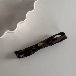 Close-up of leopard print bow hair clip with gold metal love plaque on ceramic plate