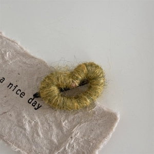 Close-up of heart-shaped hair clip featuring yellow knitted yarn texture on a black clip