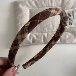 Macro detail of brown checkered headband with a gold Love oval metal plaque