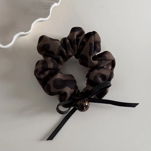 Close-up of leopard print hair scrunchie with black ribbon bow and decorative bead detail