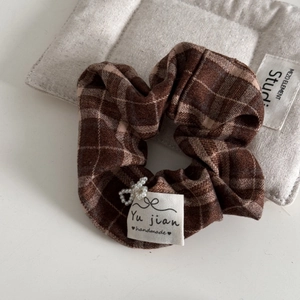 Detailed shot of a brown plaid hair scrunchie with a handmade label and pearl butterfly