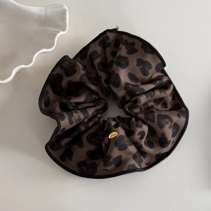 Detail of leopard print scrunchie with silk texture and a golden Love metal pendant