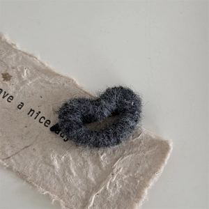 Detailed view of dark grey plush heart-shaped hair tie on rustic handmade paper