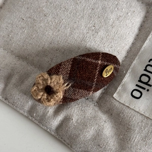 Detail of a brown plaid hair clip featuring a knitted flower and gold Love metal tag