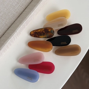 Set of 9 colorful acetate teardrop hair clips with gold handmade lettering on white surface