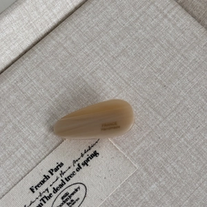 Detail of cream acetate teardrop hair clip with France Handmade engraving on linen