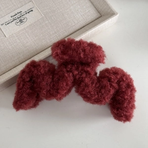 Dettaglio della morbida texture bordeaux in lana di agnello di una pinza per capelli