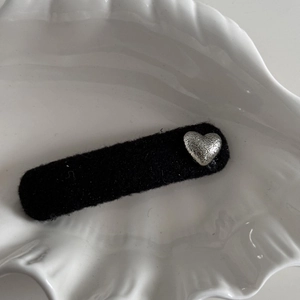 Detail of black fabric hair clip with a silver textured heart charm on a shell tray