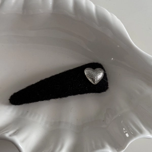Detail of silver heart charm on black fabric hair clip displayed on a ceramic shell plate