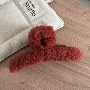 Détail d'une grande pince à cheveux en peluche rouge brique avec texture laine d'agneau