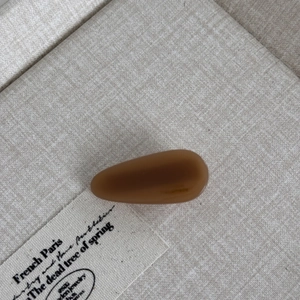Detail view of a small amber brown teardrop hair clip on a textured linen background