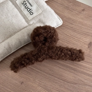 Détail d'une pince à cheveux en imitation laine d'agneau marron foncé sur bois chaud