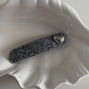Detailed view of gray fabric hair clip featuring a silver metal heart on a white shell plate