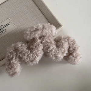 Dettaglio della trama della pinza per capelli ondulata in pile beige effetto lana