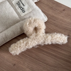 Détail macro d'une pince à cheveux en peluche beige douce sur un support en bois