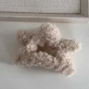 Close-up of a soft beige faux shearling star-shaped hair claw clip on a minimal tray