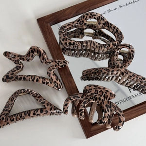 Five assorted leopard print claw clips in geometric shapes on a vintage mirror background