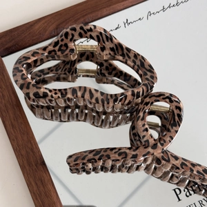Brown leopard print claw clip with golden metal spring shown on a mirror surface