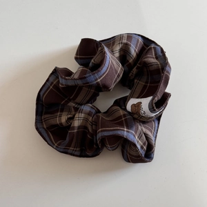Detail showing brown plaid scrunchie fabric with a small white bear patch and textile texture