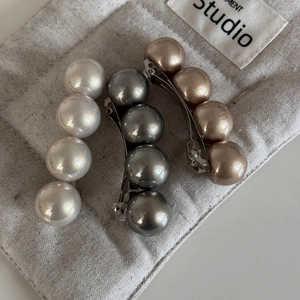 Trois barrettes à perles élégantes en blanc, gris et cuivre sur un sac en tissu