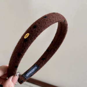 Detailed macro view of brown plush headband with black dots and golden Love metal tag