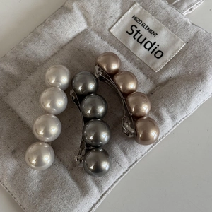 Détail de trois barrettes à perles en blanc, gris et doré champagne sur fond de tissu