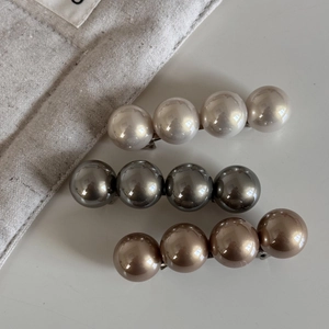 Trois barrettes à perles élégantes en crème, gris et or disposées sur un lin blanc