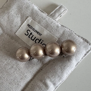 Détail macro de quatre perles champagne sur une pince à cheveux à ressort argentée