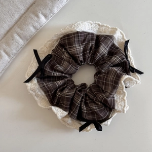 Close-up of brown plaid scrunchie with white lace trim and black ribbon bows