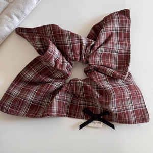 Detail of red and grey plaid scrunchie featuring a black bow and Hand Made label