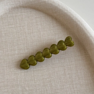 Détail d'une pince à cheveux vert olive en acétate avec sept motifs de cœur perlé
