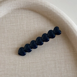 Détail de la pince à cheveux en acétate bleu marine avec sept cœurs 3D sur tissu beige