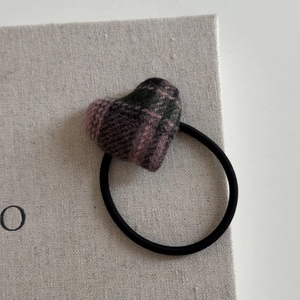 Detailed view of a plaid heart-shaped hair tie on a grey fabric textured surface