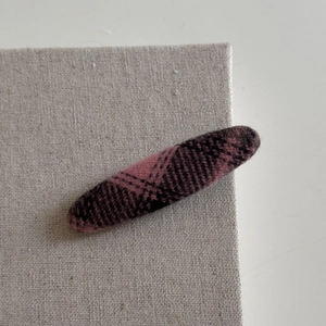 Detail view of oval hair clip featuring classic dark magenta and black plaid fabric texture