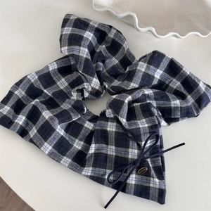 Detail eines dunkelblauen karierten Scrunchie mit Schleife und goldenem Anhänger