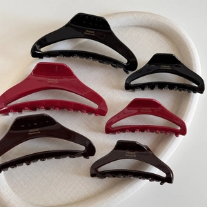 Detailed view of handmade acetate hair claws in black, red, and brown with gold logo