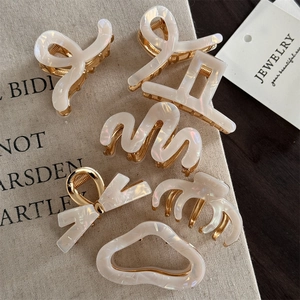 Lot de pinces à cheveux en acétate blanc nacré avec finitions dorées sur toile beige
