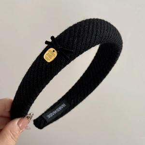 Close-up of black knitted headband with velvet bow and golden metal plate logo