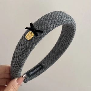 Macro detail of grey knitted headband featuring black velvet bow and golden metal tag