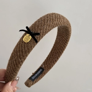 Detailed close-up of brown knit headband texture with black bow and gold metal charm