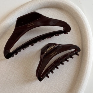 Dark brown hollow acetate hair claw clips with gold branding on beige tray