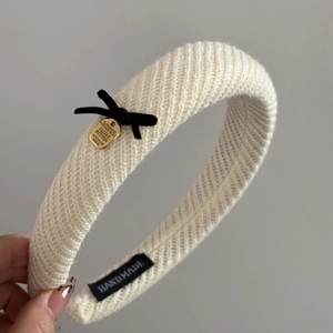 Detail of cream knit headband with black velvet bow and gold metal plate charm