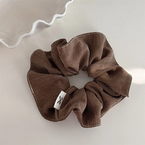 Macro detail of dark brown herringbone fabric scrunchie with cute bow label on white surface