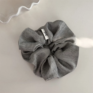Detail view of grey herringbone fabric scrunchie with a minimalist white bow tag